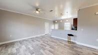 This single-story, 3-bedroom, 2-bathroom home offers a functional and modern layout designed for comfortable everyday living. The open-concept kitchen and living area serves as the heart of the home, featuring light wood-look flooring, crown molding, and a ceiling fan that enhance the bright, cohesive aesthetic. The kitchen is outfitted with rich dark wood cabinetry, granite countertops, black appliances including a refrigerator, range, and microwave, and a peninsula with pendant lighting that provides both prep space and casual seating. The spacious primary bedroom includes a ceiling fan, natural light from slatted blinds, and access to a dedicated closet. The two additional bedrooms mirror the same neutral palette, wood-look flooring, crown molding, and ceiling fans, making each a versatile and comfortable space. Both bathrooms feature tub-shower combinations with tile-look flooring and clean, neutral finishes. A hallway connects the bedrooms and bathrooms, while four closets throughout provide ample storage. The home also includes a utility room and a one-car garage, rounding out a practical and efficient floor plan. Consistent warm-gray tones and white trim carry throughout, creating a cohesive and move-in-ready interior.