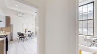 Located at 128–166 S 10th St in Newark, NJ, this thoughtfully designed one-bedroom, two-bathroom residence offers a bright, modern aesthetic throughout. The open-concept kitchen and living area serves as the heart of the home, featuring light wood-look flooring, a tray ceiling with a ceiling fan, and a wall-mounted mini-split system. The kitchen is appointed with high-gloss white upper cabinetry, warm wood-toned lower cabinets, granite countertops, stainless steel appliances, and a matte black faucet. The adjacent living area is bathed in natural light from oversized, multi-pane grid windows that frame views of the surrounding neighborhood. The bedroom is generously proportioned, showcasing soaring ceilings, dual built-in closets, a wall-mounted mini-split, and large grid windows that flood the space with daylight. Both bathrooms feature striking tile work, with mixed wood-toned and charcoal striped tiles creating a bold, contemporary design, complemented by a deep soaking tub and matte black hardware accents. Light wood-look flooring runs consistently throughout, tying the spaces together in a cohesive, airy palette. The overall ambiance is clean, bright, and modern, offering a comfortable and stylish urban living experience.
