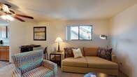 Located at 13803 SE 18th St in Vancouver, Washington, this two-floor residence offers a practical and comfortable layout across its levels, connected by a carpeted stairway with a handrail and natural light from a window landing. The living area is a welcoming space finished with carpet flooring, featuring a sliding glass door that opens to a private balcony overlooking lush greenery and mature trees, bringing the outdoors in with abundant natural light. The kitchen is well-appointed with warm honey-toned wood cabinetry, light stone-look countertops, black appliances including a range, refrigerator, and dishwasher, and durable wood-look flooring throughout. Two bedrooms provide comfortable retreats, each with carpet flooring, windows that allow natural light, and ample room for storage. The bathroom is finished with wood-look flooring, a wide vanity with stone-look countertops, warm wood cabinetry, a large mirror, and a full tub-shower combination. The upper level, as revealed in the dollhouse view, includes a spacious primary bedroom with multiple windows and dedicated dresser space. Throughout the residence, the neutral color palette and warm finishes create a cohesive and inviting atmosphere.