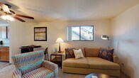 Located at 13803 SE 18th St in Vancouver, Washington, this two-floor residence offers a practical and comfortable layout across its levels, connected by a carpeted stairway with a handrail and natural light from a window landing. The living area is a welcoming space finished with carpet flooring, featuring a sliding glass door that opens to a private balcony overlooking lush greenery and mature trees, bringing the outdoors in with abundant natural light. The kitchen is well-appointed with warm honey-toned wood cabinetry, light stone-look countertops, black appliances including a range, refrigerator, and dishwasher, and durable wood-look flooring throughout. Two bedrooms provide comfortable retreats, each with carpet flooring, windows that allow natural light, and ample room for storage. The bathroom is finished with wood-look flooring, a wide vanity with stone-look countertops, warm wood cabinetry, a large mirror, and a full tub-shower combination. The upper level, as revealed in the dollhouse view, includes a spacious primary bedroom with multiple windows and dedicated dresser space. Throughout the residence, the neutral color palette and warm finishes create a cohesive and inviting atmosphere.