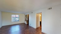 This two-story residence is designed with a practical and straightforward layout spread across two distinct levels. The main floor features rich, dark wood-style flooring throughout the open living area, which is brightened by a window that allows natural light to fill the space. A staircase with a white railing connects the main level to the upper floor and is visible from the living area, contributing to the home's open feel. Adjacent to the living space, a door leads to a bathroom on the main level. The kitchen is equipped with dark espresso-toned cabinetry, stone-patterned countertops, a double stainless steel sink, and stainless steel appliances, offering ample storage and workspace.

The upper level transitions to neutral-toned carpeting throughout the bedrooms, providing a softer underfoot feel. The bedrooms are well-proportioned, with one featuring a walk-in closet with shelving and an additional door providing access to other areas of the upper floor. A second bedroom offers a window with outdoor views. The bathroom on this level includes a soaking tub and shower combination with tiled surround and brushed nickel fixtures. A tall stairwell with a high window adds architectural interest and draws in additional natural light.