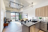 Located at 1600 Lauzon Rd in Windsor, Ontario, this contemporary 2-bedroom, 2-bathroom unit showcases a thoughtfully designed industrial-chic aesthetic across a single floor. The open-concept kitchen and living area is a striking centerpiece, featuring exposed concrete ceilings with bold track lighting, a statement chandelier, and wide-plank light wood flooring. The kitchen is outfitted with warm wood cabinetry, a geometric tile backsplash, dark stone countertops, a large island with seating, and a full suite of stainless steel appliances. Sliding glass doors flood the living space with natural light and provide direct access to a private balcony with glass-panel railings and open outdoor views. The bedrooms offer a calm retreat, with the primary bedroom generously proportioned and supported by a dedicated closet. Both bathrooms are finished with large-format tiles, glass-enclosed showers, and terrazzo-style flooring, reflecting a clean, modern sensibility. A dedicated laundry room houses a full-size stacked washer and dryer alongside a utility sink. Exposed ductwork and concrete ceilings throughout reinforce the unit's urban loft character, while light-filled rooms and contemporary finishes create a polished, livable space.