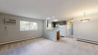 This single-floor unit is thoughtfully laid out with an open-concept design that connects the living area and kitchen. The spacious living room features neutral-toned carpet, light gray walls, and a baseboard heating system, with a large window that invites natural light and outdoor views. A private entry door provides direct access to this area.

The kitchen is a standout feature, equipped with dark espresso cabinetry, granite countertops, a white subway tile backsplash, and gray tile flooring. A peninsula with bar-height overhang creates a natural division between the kitchen and living space, while white appliances—including a refrigerator, range, microwave, and dishwasher—complete the functional layout. A window above the sink adds additional natural light.

The bedrooms are carpeted and painted in soft gray tones, each featuring wall-mounted air conditioning units and baseboard heaters for year-round climate control. One bedroom includes a built-in closet with a rod and shelf for storage.

The bathroom is clean and modern, featuring large-format tile flooring, white cabinetry with granite countertops, a wall-mounted cabinet for additional storage, and a shower with tiled surround.