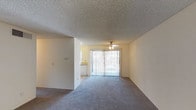 Located at 6304 Rancho Mission Road, Unit #177 at The Athens in San Diego, this single-floor residence offers a practical and comfortable layout suited for everyday living. The main living area is open and spacious, featuring wall-to-wall carpeting that adds warmth underfoot. A ceiling fan is centrally positioned overhead, providing both airflow and a subtle decorative touch. The room is finished with a textured ceiling and clean, neutral-toned walls that offer a blank canvas for personalization. A large sliding glass door fitted with vertical blinds allows natural light to pour into the living space while providing direct access to an outdoor area, enhancing the sense of openness. Adjacent to the living area, a glimpse of the kitchen reveals white appliances and light-toned cabinetry, reflecting a clean and functional design. The overall layout is thoughtfully arranged, with the living and kitchen areas flowing seamlessly into one another. The neutral color palette and carpeted flooring create a cohesive, welcoming ambiance throughout the space. This residence combines functionality with comfortable living in one of San Diego's well-established residential communities.