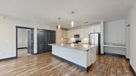 Located at 2107 Lothric Way in Murfreesboro, TN, this well-appointed 2-bedroom, 2-bathroom residence offers a thoughtfully designed single-floor layout with modern finishes throughout. The open-concept kitchen and living area serves as the heart of the home, anchored by a large central island topped with a stone countertop and flanked by sleek white cabinetry that extends to the ceiling. Stainless steel appliances, a subway tile backsplash, and stylish pendant lighting complete the contemporary kitchen aesthetic. Warm wood-look flooring flows throughout the main living areas, complemented by dark-trimmed doors and baseboards that add a bold contrast to the light-toned walls. The spacious living room receives generous natural light through large windows and provides direct access to a private balcony. Both bedrooms are carpeted and include ceiling fans and ample natural light. The primary bedroom features its own walk-in closet with wire shelving, while additional closets throughout the unit offer plentiful storage. The bathrooms are finished with large-format marble-look tile, including an elegant tub-shower surround. A dedicated hallway connects the living spaces to the private quarters, contributing to a well-organized and functional floor plan.