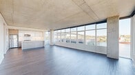 This well-appointed two-bedroom, two-bathroom residence showcases a striking blend of industrial and contemporary design across a generously sized single floor. The open-concept living and kitchen area is the heart of the home, anchored by dramatic floor-to-ceiling windows that span the full length of the space, flooding the interior with natural light and framing sweeping waterfront views of a river, bridge, and cityscape beyond. Exposed concrete ceilings add an industrial character throughout, complemented by sleek hardwood-style flooring in the main living areas. The modern kitchen features a large central island with a clean quartz countertop, high-gloss white upper cabinetry, wood-toned lower cabinetry, and a full suite of stainless steel appliances. A long, well-lit hallway with recessed lighting connects the living areas to the private quarters. Both bedrooms are carpeted and benefit from the exposed concrete ceiling aesthetic, with the primary bedroom offering direct access to an en-suite bathroom and outdoor views. The bathrooms are finished with neutral tile flooring, contemporary vanities, and tub-shower combinations. Each bedroom is served by a dedicated closet with built-in shelving and hanging rods, providing ample storage throughout.