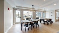 Located at 1557 Ellinwood St in Des Plaines, Illinois, this single-floor communal space offers a thoughtfully designed layout that blends comfort, functionality, and contemporary style. The open floor plan connects several distinct zones, each serving a unique purpose while maintaining a cohesive aesthetic throughout.

The kitchen is a standout feature, outfitted with deep navy cabinetry, dark countertops, a stainless steel gas range with a hood vent, and a white subway tile backsplash. An open wood shelf adds warmth, while a large island with a light countertop anchors the space. Patterned encaustic floor tiles near the kitchen entrance provide a decorative accent, and industrial-style pendant lighting overhead completes the look.

The dining area accommodates multiple seating arrangements beneath Edison bulb pendant fixtures. Large windows and a glass door flood the space with natural light and offer direct views of and access to an outdoor terrace with landscaping and pergola structures.

Multiple lounge areas are distributed throughout, featuring accent chairs, sofas, and entertainment options including wall-mounted televisions. A game area with a billiards table adds a recreational element. Hardwood flooring and neutral-toned walls unify the space, creating a welcoming and versatile environment.