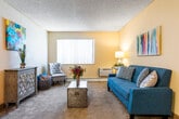 This single-floor residence offers a thoughtfully arranged layout that maximizes comfort and functionality throughout. The living area serves as the heart of the home, featuring plush wall-to-wall carpeting, warm neutral-toned walls, and a textured ceiling with a ceiling fan overhead. A large window with vertical blinds allows natural light to fill the space, while a baseboard heating unit ensures year-round comfort. The room provides ample space for seating and a dining area, with hardwood-style flooring defining the entryway and dining nook nearby. The galley-style kitchen is efficiently designed, showcasing warm wood cabinetry, dark granite-style countertops, hardwood-style flooring, and black appliances including a range and dishwasher. The bedroom is a restful retreat, carpeted and generously sized to accommodate a large bed comfortably, with a window allowing natural light and a built-in closet offering practical storage. The bathroom is neatly appointed with warm wood vanity cabinetry, a white countertop with a single-basin sink, overhead storage cabinets, and a shower-tub combination. Throughout the residence, a cohesive warm color palette and consistent finishes create a welcoming and livable atmosphere.