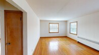 This two-bedroom, one-bathroom unit in Wauwatosa, Wisconsin is laid out entirely on a single floor, offering a straightforward and functional floor plan. Warm hardwood flooring flows consistently throughout the living areas and both bedrooms, complemented by wood-trimmed windows and matching baseboards that lend a cohesive, classic character to the space.

The living room is generously proportioned, featuring two windows that invite ample natural light and provide views of the surrounding exterior. A radiator unit provides heating, maintaining the home's traditional character. The second bedroom mirrors this setup with its own window and radiator, while the primary bedroom offers a slightly larger footprint with an additional window and access to a closet.

The kitchen is equipped with a white range and features light tile flooring, providing a practical workspace distinct from the hardwood areas. The full bathroom retains its vintage charm with pink wall tile surrounding the tub-shower combination, a mosaic tile floor in soft pastel tones, a white vanity, and a frosted window above the tub for natural light and privacy.

Overall, the unit presents a well-maintained, classic aesthetic with consistent warm-toned wood details and functional room layouts throughout.