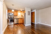 Located at 3936 Pennsylvania Ave in Kansas City, MO, this single-floor residence offers a thoughtfully designed layout with consistent dark hardwood flooring connecting each room. The open living area is bright and inviting, featuring a large sliding glass door with vertical blinds that brings in generous natural light, complemented by a textured ceiling and track lighting. The kitchen is well-equipped with stainless steel appliances, including a range, microwave, and refrigerator, along with warm honey-toned wood cabinetry, dark granite countertops, a stainless steel sink, and a diagonal tile backsplash that adds visual interest. A stacked washer and dryer unit is conveniently housed in a dedicated laundry alcove just off the main living space. The bedroom features two windows that fill the room with natural light, a decorative palm-leaf ceiling fan, and a mirrored closet. A distinctive decorative column frames the passage into the en-suite bathroom, which is appointed with diamond-patterned tile walls, a navy vanity with a white countertop, and elegant sconce lighting. Throughout the home, clean white baseboards and neutral wall tones create a cohesive and move-in ready aesthetic.