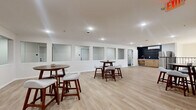 Located at 3425 Eischen Ct in Duluth, MN, this single-floor community amenity space offers a well-appointed and versatile environment designed for gathering and socializing. The layout flows between two distinct areas, each finished with light-toned luxury vinyl plank flooring that gives the space a clean, modern aesthetic throughout.

The lounge area is bright and welcoming, featuring large windows that invite abundant natural light and offer views of the surrounding exterior. Mid-century modern-inspired seating, including cushioned sofas and a round coffee table, create a comfortable and stylish setting for relaxation or casual conversation. A staircase with a sleek black metal railing connects this area to the rest of the building.

The open gathering room is spacious and versatile, lined with recessed lighting and white walls accented by a row of framed window openings that add architectural interest. High-top bistro tables with upholstered stools are arranged throughout, making the area ideal for social events or communal use.

Adjacent to the gathering room is a functional kitchenette, highlighted by a bold black hexagonal tile backsplash, natural wood cabinetry, a stainless steel refrigerator, and a wall-mounted mini-split unit. This well-designed amenity space combines practicality with contemporary style, creating an inviting hub for residents at this Duluth community.