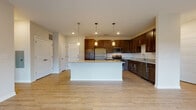 Located at 915 Main St in Mukwonago, WI, this well-appointed single-floor residence offers a thoughtfully designed open-concept layout with modern finishes throughout. The kitchen serves as the heart of the home, showcasing rich dark cabinetry, granite countertops, a large center island with pendant lighting above, and a full suite of stainless steel appliances including a refrigerator, range, microwave, and dishwasher. Light wood-tone flooring runs throughout the main living areas, creating a bright and cohesive aesthetic. The spacious living room is filled with natural light from a large sliding window and provides direct access to a private balcony overlooking a scenic, tree-lined landscape. Bedrooms are carpeted for comfort, with one featuring an en-suite bathroom that leads directly into a walk-in closet equipped with built-in shelving and hanging rods. Bathrooms are finished with granite-top dark wood vanities, tile flooring, and a full tub-shower combination. A second bathroom mirrors the same quality finishes. Recessed lighting and clean neutral wall tones contribute to a polished, move-in-ready environment throughout this inviting single-level residence.