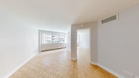 Located at 3450-3460 Rue Drummond in the heart of Montréal, this one-bedroom, one-bathroom unit offers a practical and well-organized layout across a single floor. The living area is bright and welcoming, featuring classic parquet wood flooring in a herringbone-style pattern and a large window that allows natural light to fill the space while offering views of the surrounding cityscape. A baseboard heating unit runs along the window wall, ensuring year-round comfort. The bedroom continues the warm parquet flooring and includes a built-in closet, providing functional storage within a cozy, well-proportioned space. The kitchen is efficiently designed in an L-shaped configuration, outfitted with white cabinetry extending to the ceiling for ample storage, warm wood-toned countertops, a stainless steel sink, and white appliances including a refrigerator and electric range. Light ceramic tile flooring grounds the kitchen area. A hallway connects the rooms and leads to the bathroom, which features a full-sized soaking tub with an overhead shower, white subway tile surround, chrome fixtures, and grab bars — combining both style and accessibility. The overall aesthetic is clean and neutral, with white walls and trim throughout, offering a move-in-ready canvas in a prime Montréal location.