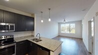 This well-appointed single-floor residence offers a thoughtfully designed open-concept layout that seamlessly connects the kitchen and living areas. The kitchen is a standout feature, showcasing dark espresso cabinetry that extends to the ceiling, granite countertops, and a full suite of stainless steel appliances including a refrigerator, range, and built-in microwave. A kitchen island with a granite surface and undermount sink serves as both a functional workspace and a casual dining spot, accented by stylish pendant lighting overhead. The living area is bright and airy, benefiting from large windows that invite natural light and offer views of the surrounding greenery. Hardwood-style flooring runs throughout the main living spaces, adding warmth and continuity to the open floor plan. The bedrooms provide a comfortable retreat, with one featuring plush carpeting and a ceiling fan, and another showcasing hardwood-style flooring and a large window with outdoor views. The bathroom is finished with matching granite countertops, dark cabinetry, a dual-sink vanity, and well-lit mirrors. Additional conveniences include an in-unit stacked washer and dryer. The overall ambiance is clean, contemporary, and move-in ready.