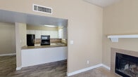 This single-floor, 2-bedroom, 1-bathroom residence offers a functional and cohesive layout finished in warm neutral tones throughout. The living room serves as the central gathering space, featuring a tiled fireplace with a white mantel, vaulted ceilings that enhance the sense of openness, carpet flooring, and a sliding glass door with vertical blinds that allows natural light to filter in. The kitchen is designed with efficiency in mind, accessible via an open pass-through counter from the living area. It is equipped with white cabinetry, a double sink, a black refrigerator, an electric range with overhead microwave, and ample counter space — all finished with easy-care hard surface flooring. The primary bedroom is generously sized with carpet flooring, a window for natural light, and a closet. The second bedroom mirrors this comfortable setup, also featuring carpet, a window with blinds, and an open closet with built-in shelving for ample storage. The bathroom includes a wide vanity with a single basin sink, a speckled countertop, white cabinetry, and a large wall mirror. Throughout the home, consistent warm beige walls and clean white trim contribute to a cohesive, move-in-ready aesthetic.