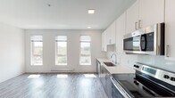 This single-floor unit presents a thoughtfully designed, modern living space with a clean, contemporary aesthetic carried consistently throughout. The open-concept layout seamlessly connects the kitchen and living area, creating a bright, airy environment enhanced by multiple large windows that invite an abundance of natural light and offer views of the surrounding neighborhood.

The kitchen is well-appointed with sleek white upper cabinetry paired with wood-toned lower cabinets, light quartz countertops, and a full suite of stainless steel appliances, including a range, microwave, dishwasher, and refrigerator. Wood-look plank flooring runs throughout the space, adding warmth and visual continuity across every room.

The bathroom is finished to a high standard, featuring a white single-sink vanity with ample drawer storage, a large mirror with overhead lighting, and a walk-in shower. The neutral white palette and wood-look tile flooring give the space a crisp, spa-like quality.

A dedicated laundry area houses a stacked washer and dryer unit alongside wire shelving, providing practical storage and organizational convenience. Recessed lighting throughout the unit complements the natural light, ensuring a well-lit interior at all hours. The overall ambiance is modern, clean, and move-in ready.