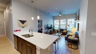Located at 1900 State Highway 25 in Gainesville, FL, this single-story residence offers a thoughtfully designed open-concept layout with modern finishes throughout. The kitchen serves as the centerpiece of the living space, featuring a large island with a white quartz countertop, an undermount double sink, pendant lighting, dark wood cabinetry, stainless steel appliances, and bar seating — ideal for both cooking and casual dining. The kitchen flows seamlessly into the living area, which is bathed in natural light from a bank of large windows and equipped with a ceiling fan. Light wood-style flooring runs throughout the main living areas, enhancing the bright, airy atmosphere. The living room offers ample space for comfortable seating arrangements and provides views to the outdoors. The bedrooms are carpeted and well-proportioned, each featuring windows that allow natural light to filter in. The bathrooms are cleanly appointed with dark wood or navy vanity cabinets, white countertops, large mirrors, and modern fixtures. One bathroom includes a shower-tub combination. The overall design aesthetic is contemporary and cohesive, with neutral tones and clean lines creating a welcoming, functional living environment throughout the single-floor layout.