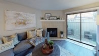 This single-floor residence offers a thoughtfully designed layout that balances comfort and functionality across its key living areas. The living room serves as the heart of the home, anchored by a tile-surround fireplace with a clean white mantel and complemented by wood-look flooring and a sliding glass door that opens to a private outdoor patio, filling the space with natural light. Adjacent to the living area, the dining space features a round wood table and is connected to the kitchen via a pass-through counter with bar seating. The kitchen is well-equipped with white shaker cabinetry, grey countertops, stainless steel appliances including a refrigerator, range, microwave, and dishwasher, along with a deep single-basin sink. Two bedrooms offer carpeted flooring, neutral walls, and windows with outdoor views. The primary bedroom includes a sliding-door closet, while the secondary bedroom provides ample space for furniture and storage. A full bathroom features a tub-shower combination with built-in shelving, dark wood-look flooring, and a dark countertop vanity. A separate powder room with wood-look flooring and a round mirror adds convenience. Textured ceilings are present throughout, contributing to the home's warm, residential character.