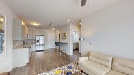 Located at 7740 Midtown Market Avenue in Raleigh, NC, this single-floor unit offers a well-designed, open-concept layout with modern finishes throughout. The living area is bright and welcoming, featuring wood-look flooring, a ceiling fan, and a glass-paned door that brings in natural light and provides views of the surrounding neighborhood. The kitchen is outfitted with light wood cabinetry, granite countertops, a white subway tile backsplash, and a full suite of stainless steel appliances including a range, microwave, dishwasher, and French door refrigerator. A breakfast bar with seating connects the kitchen to the living space, enhancing the open feel. The bedroom is a calm retreat with neutral tones, a large window, and a walk-in closet with built-in shelving. The bathroom features a granite-topped vanity with undermount sink, light wood cabinetry, and a glass-enclosed walk-in shower with white tile surround. A dedicated in-unit laundry area accommodates a stacked washer and dryer. Consistent wood-look flooring flows throughout the space, tying together the clean, contemporary aesthetic of the entire unit.