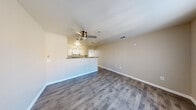 Located at 121 N 15th St in Las Vegas, NV, this one-bedroom, one-bathroom unit offers a thoughtfully arranged single-floor layout that maximizes every inch of available space. The open-concept living and kitchen area serves as the heart of the unit, where durable wood-style flooring extends throughout, creating a cohesive and easy-to-maintain surface. A ceiling fan centered above the living area provides both function and a finishing touch to the textured ceiling. The kitchen is designed in a galley configuration, featuring white cabinetry, dark speckled countertops, a double-basin sink, and white appliances including a range with overhead microwave and a full-size refrigerator. A peninsula counter separates the kitchen from the living space, adding a subtle architectural division while maintaining an open feel. The bedroom is carpeted for comfort and benefits from a large window that invites natural light. A sliding-door closet with a full-width rod and shelf provides practical storage. A hallway connects the main living areas to the bedroom and bathroom, which includes a single-sink vanity with dark countertop, a combined tub and shower, and wood-style flooring that ties back to the rest of the unit's design. Clean, neutral tones throughout give the space a bright and functional character.