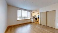 Located on the sixth floor at 4744 12th Avenue Northeast in Seattle's University District, this efficiently designed studio unit makes excellent use of its compact footprint. The open-plan living, dining, and kitchen area forms the heart of the space, bathed in natural light from a large multi-pane window fitted with horizontal blinds that frame elevated views of the surrounding Seattle cityscape. Light-toned hardwood-style flooring runs continuously throughout, lending warmth and visual cohesion to the entire unit. The kitchen is well-appointed with light maple cabinetry, granite countertops with a breakfast bar overhang, and a full suite of stainless steel appliances including a range, microwave, dishwasher, and refrigerator. Track lighting overhead ensures the kitchen remains bright and functional. The entry area features a sliding-door closet for convenient storage, alongside a keypad-secured front door. A full bathroom includes a soaking tub and shower combination with clean white surround. The unit's crisp white walls and neutral palette create a clean, modern ambiance throughout, making it a practical and comfortable space in a highly walkable Seattle neighborhood.