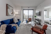 Located at 331 Westport Rd in Kansas City, MO, this single-floor unit offers a thoughtfully designed open-concept layout with modern finishes throughout. The living area is a standout space, anchored by large floor-to-ceiling sliding glass doors that lead to a private balcony overlooking the surrounding Westport neighborhood. Natural light fills the room, complementing the wood-style flooring and neutral wall tones that create a clean, contemporary aesthetic.

The kitchen is well-appointed with white cabinetry, subway tile backsplash, stainless steel appliances including a range, microwave, and refrigerator, and a generous island with seating. Recessed lighting and under-cabinet illumination add a polished touch to the space.

The bedroom is carpeted for comfort and features a large window that frames outdoor views, allowing ample natural light. The adjoining bathroom includes a white vanity with quartz-style countertops, wood-tone flooring, and direct access to the bedroom, functioning as an en-suite arrangement.

Overall, the unit presents a cohesive modern design with a neutral palette, quality fixtures, and a functional layout that balances open living and private spaces effectively.
