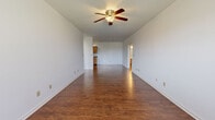 This single-floor residence offers a practical and comfortable layout designed for everyday living. The open living and dining area is a standout feature, finished with rich, dark wood-look flooring that extends throughout the common spaces. A ceiling fan with a built-in light fixture provides both comfort and illumination, while a window allows natural light to brighten the room. The space flows seamlessly toward the kitchen and additional rooms beyond.

The galley-style kitchen is efficiently designed with warm honey-toned wood cabinetry lining both walls, complemented by dark countertops and a double-basin sink. White appliances, including a refrigerator, electric range, and over-the-range microwave, are neatly integrated into the layout. Recessed lighting overhead ensures the kitchen remains well-lit.

The bedrooms feature plush neutral carpeting and windows with blinds that invite natural light and outdoor views. The layout accommodates multiple sleeping areas, each offering a quiet, comfortable retreat.

Two bathrooms serve the residence, each featuring wood-look flooring, warm wood vanity cabinetry, light countertops, and a large mirror above the sink. One bathroom includes a shower with a curtain enclosure.

A dedicated laundry room is equipped with washer and dryer hookups, a dryer vent connection, wire shelving above, and ample wall outlets, providing functional in-unit laundry convenience.