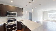 This modern 2-bedroom, 2-bathroom residence offers a thoughtfully designed single-level layout that maximizes functionality and style. Rich hardwood flooring flows throughout the main living areas, anchoring the open-concept design that connects the kitchen, dining, and living spaces seamlessly.

The kitchen is a standout feature, equipped with stainless steel appliances including a double-oven range, built-in microwave, side-by-side refrigerator, and dishwasher. Dark espresso cabinetry with ample storage contrasts elegantly with the white quartz countertops and peninsula island, which is illuminated by sleek cylindrical pendant lights. A large window at the far end of the living area floods the space with natural light and provides outdoor views.

The hallway leads to two well-proportioned bedrooms, each featuring hardwood flooring and closet storage. The primary bedroom offers a generous footprint with its own dedicated closet, while the secondary bedroom includes a ceiling fan and built-in closet shelving. Both bathrooms are finished in a clean, contemporary style with tile flooring and modern vanities.

Additional highlights include three closets for abundant storage, a dedicated in-unit laundry area with a stacked washer and dryer, and a neutral color palette throughout that enhances the bright, airy ambiance of the entire space.