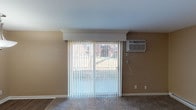 Located at 5107 Colerain Ave in Cincinnati, Ohio, this single-floor unit offers a practical and well-appointed layout across several comfortable living spaces. The open-concept living area features neutral-toned walls, plush carpeting, and a sliding glass door dressed with vertical blinds that allows natural light to filter in and provides a view of the surrounding exterior. A wall-mounted air conditioning unit ensures year-round comfort in this space.

The kitchen is thoughtfully designed with rich, dark-stained cabinetry featuring shaker-style doors, light granite-look countertops, and stainless steel appliances including an electric range and a full-size refrigerator. Warm hardwood-style flooring and a central flush-mount ceiling light complete the kitchen's modern aesthetic. A peninsula counter connects the kitchen to the main living area, creating a cohesive, open flow.

The bedrooms are carpeted and finished in warm neutral tones, each benefiting from natural light through windows with blinds. One bedroom includes a sliding closet with a rod and shelf for storage, as well as a wall-mounted AC unit and baseboard heating. Additional bedrooms also feature baseboard heating and generous window placement for natural light.

The bathroom is clean and functional, featuring tile flooring, a full-size soaking tub and shower combination with a curved rod, and classic white fixtures throughout.
