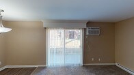 Located at 5107 Colerain Ave in Cincinnati, Ohio, this single-floor unit offers a practical and well-appointed layout across several comfortable living spaces. The open-concept living area features neutral-toned walls, plush carpeting, and a sliding glass door dressed with vertical blinds that allows natural light to filter in and provides a view of the surrounding exterior. A wall-mounted air conditioning unit ensures year-round comfort in this space.

The kitchen is thoughtfully designed with rich, dark-stained cabinetry featuring shaker-style doors, light granite-look countertops, and stainless steel appliances including an electric range and a full-size refrigerator. Warm hardwood-style flooring and a central flush-mount ceiling light complete the kitchen's modern aesthetic. A peninsula counter connects the kitchen to the main living area, creating a cohesive, open flow.

The bedrooms are carpeted and finished in warm neutral tones, each benefiting from natural light through windows with blinds. One bedroom includes a sliding closet with a rod and shelf for storage, as well as a wall-mounted AC unit and baseboard heating. Additional bedrooms also feature baseboard heating and generous window placement for natural light.

The bathroom is clean and functional, featuring tile flooring, a full-size soaking tub and shower combination with a curved rod, and classic white fixtures throughout.
