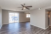 This single-floor unit offers a practical and functional layout designed for comfortable everyday living. The flooring is consistent throughout, featuring durable grey vinyl plank that adds a modern, cohesive look to each room.

The living area is generously sized, with neutral grey walls, a textured ceiling, and a ceiling fan with a light fixture that provides both air circulation and overhead lighting. A front entry door opens directly into this open space, which benefits from a bright, airy feel.

The galley-style kitchen is efficiently arranged with warm wood cabinetry, white countertops, and black appliances including an electric range with a ventilation hood, a dishwasher, and a full-size refrigerator. A window in the adjacent dining area allows natural light to fill the space.

Two well-proportioned bedrooms feature the same grey vinyl plank flooring, neutral-toned walls, and textured ceilings, offering versatile spaces suitable for a variety of furniture arrangements.

The bathroom includes a single-sink vanity with warm wood cabinetry and a white countertop, a large mirror, and a tiled tub-shower combination. A hallway connects the bathroom to the rest of the unit, with additional storage visible nearby. The overall aesthetic is clean, updated, and move-in ready.