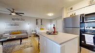 This studio unit offers a thoughtfully designed open-concept layout that seamlessly integrates the kitchen, living, and sleeping areas into one cohesive space. Light hardwood flooring runs throughout, lending warmth and visual continuity across every zone.

The kitchen is a standout feature, outfitted with crisp white shaker cabinetry accented by matte black hardware, a classic white subway tile backsplash, and light stone countertops. A central island provides additional prep space and doubles as a casual dining area with bar-style seating. Stainless steel appliances — including a full-size refrigerator, range, microwave, and dishwasher — complete the functional and polished kitchen space. A large window floods the kitchen with natural light.

The open living area accommodates both a lounge and sleeping space with ease. A ceiling fan overhead provides comfort, while a natural-light window with blinds brings in soft, diffused daylight. The layout allows for flexible furniture arrangement, making the space feel organized and livable despite its compact footprint.

The bathroom features a combined shower and tub enclosure with a clean white curtain, a white vanity, and continued hardwood-style flooring, maintaining the consistent aesthetic found throughout the unit. The overall ambiance is modern, clean, and functional.