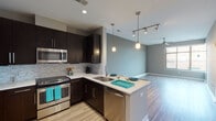 This contemporary single-floor residence showcases a thoughtfully designed open-concept layout that seamlessly connects the kitchen, dining, and living areas. The kitchen is a standout feature, equipped with sleek dark espresso cabinetry, stainless steel appliances including a refrigerator with ice maker, range, microwave, and dishwasher, complemented by a mosaic tile backsplash and crisp white countertops. A peninsula with bar seating and elegant pendant lighting serves as the central hub, making it ideal for both casual dining and entertaining. Track lighting and recessed ceiling lights further enhance the kitchen and living areas. The open living space is finished with warm wood-look flooring and neutral gray walls, creating a bright and airy atmosphere. A ceiling fan adds both function and style to the room, which benefits from natural light through large windows. The bedrooms are generously proportioned, featuring a mix of wood-look flooring and plush carpet, ceiling fans, and large windows that allow ample natural light. The bathroom is finished with large-format stone-look tile on both the floors and shower surround, a soaking tub, and a dark vanity topped with a granite-style countertop, offering a clean and refined aesthetic throughout.