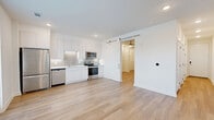 Located at 1 Riverside Ave in Jacksonville, Florida, this efficiently designed one-bedroom, one-bathroom unit offers a clean, modern aesthetic with consistent light wood flooring and crisp white walls throughout. The open-concept kitchen and living area serves as the heart of the space, featuring flat-front white cabinetry, a gray tile backsplash, stainless steel appliances including a refrigerator, range, microwave, and dishwasher, plus a sliding barn door that connects to the bedroom wing. Natural light filters in through a glass door leading to an outdoor balcony, enhancing the bright, airy feel of the main living area. The bedroom is a well-proportioned retreat with a ceiling fan, recessed lighting, and direct access to the hallway. A long, well-lit hallway leads to two closets and a dedicated laundry area with an in-unit washer. The bathroom is finished in a clean, contemporary style with a full soaking tub and shower combination, white tile surround, a floating vanity with ample drawer storage, and a large mirror. Recessed lighting throughout the unit maintains a sleek, uncluttered ambiance, making this an intelligently laid-out and well-appointed urban residence.