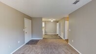 This single-story unit in Albany, Georgia, offers a practical and well-organized layout designed for comfortable everyday living. The interior is finished with neutral gray and taupe tones throughout, creating a cohesive and understated aesthetic across all rooms.

The living area is generously proportioned, featuring wall-to-wall carpet, a textured ceiling, and a sliding glass door that opens to a private balcony, allowing natural light to fill the space and providing views of the surrounding exterior. The entryway transitions smoothly between carpeted and wood-look vinyl flooring, marking the boundary between the living and kitchen zones.

The kitchen is efficiently designed in a galley configuration, featuring white cabinetry, light granite-style countertops, a stainless steel sink, and white appliances including a refrigerator and electric range. Wood-look vinyl flooring runs throughout the kitchen, adding durability to the workspace.

The bedrooms are carpeted and finished with the same neutral palette, with one room featuring a ceiling fan with light fixture and a window that brings in natural light. Closet storage is also present within the unit.

The bathroom includes a full tub and shower combination, a toilet, and a vanity with matching countertop, finished with wood-look flooring for easy maintenance.