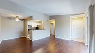This single-floor residence offers a well-designed open-concept layout that seamlessly connects the living area and kitchen. Rich, dark hardwood-style flooring runs throughout the main living spaces, creating a warm and cohesive aesthetic. The living area is generously proportioned, bathed in natural light from a large sliding glass door that opens to a private balcony overlooking a green outdoor setting — an inviting feature for relaxation or fresh air.

The kitchen is positioned behind a raised peninsula counter, offering a practical pass-through design that maintains visual openness to the living area. It is equipped with stainless steel appliances, including a microwave, electric range, and refrigerator, complemented by white cabinetry with brushed nickel hardware and dark granite-style countertops. Light tile flooring grounds the kitchen space distinctly from the main living area.

The bedroom is a comfortable, carpeted retreat featuring a ceiling fan with light fixture and a window that brings in natural light. A full bathroom includes a tub and shower combination with clean white tile surround and brushed nickel fixtures. A hallway connects the rooms, providing a logical and functional flow throughout the residence. Overall, the space presents a clean, neutral palette with practical finishes throughout.