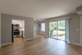 Located at 48 Washington St in Santa Clara, California, this two-bedroom, one-bathroom residence offers a well-designed single-floor layout with a clean, modern aesthetic throughout. The open living room is finished with light hardwood flooring and soft gray walls, creating a bright and airy atmosphere. A sliding glass door connects the living area to the outdoors, allowing abundant natural light and views of the lushly landscaped community grounds, which feature mature trees, manicured hedges, and a shared patio area. The kitchen is thoughtfully designed with white shaker cabinetry, white quartz countertops, a peninsula with a built-in sink, and a full suite of stainless steel appliances including a refrigerator, range, microwave, and dishwasher. A skylight adds additional brightness to the kitchen area. Both bedrooms are carpeted for comfort; the primary bedroom is generously sized and features a ceiling fan, multiple windows with natural light, and a wide built-in closet with open shelving. The second bedroom is cozy with a window overlooking the exterior. The bathroom is well-appointed with a full tub-shower combination, white tile surround, hardwood-style flooring, and built-in storage cabinetry. A connecting hallway ties the layout together efficiently.