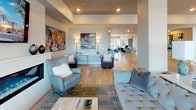 This single-floor social lounge is a thoughtfully designed communal space that seamlessly blends comfort and modern sophistication. The open-plan layout connects a fully equipped kitchen with expansive lounge and seating areas, creating an inviting environment for gathering and socializing.

The kitchen is a standout feature, outfitted with stainless steel appliances including a gas cooktop, double wall oven, and built-in dishwasher. Crisp white cabinetry, quartz countertops, and a large central island with bar seating define the space, while an eye-catching white Moroccan-patterned tile backsplash and open floating shelves add a decorative touch. Light hardwood flooring runs throughout, tying the entire space together.

The lounge areas are elegantly appointed with contemporary furniture, including leather accent chairs, a tufted sofa, and a marble-topped coffee table. A sleek, elongated linear fireplace serves as a focal point beneath a wall-mounted flat-screen television. Vibrant abstract artwork is displayed throughout, lending color and personality to the neutral palette. Large floor-to-ceiling windows and glass doors flood the interior with natural light and provide direct views of an outdoor terrace area. Structural columns punctuate the open floor plan, adding architectural interest while maintaining the spacious, airy feel of this well-appointed communal lounge.
