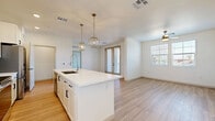 Located at 4353 E Elliot Rd in Gilbert, AZ, this well-appointed 2-bedroom, 2-bathroom single-story home offers a clean, modern aesthetic with thoughtful design throughout. The open-concept kitchen and living area serves as the heart of the home, anchored by a central island with a crisp white quartz countertop, an integrated sink with a gooseneck faucet, and stylish gold geometric pendant lights. The kitchen features white shaker cabinetry extending to the ceiling, a subtle tile backsplash, and stainless steel appliances including a French door refrigerator, range, and microwave. Light wood-look flooring runs through the main living areas, complementing the bright, neutral color palette. The living area benefits from natural light through windows and French doors, with a ceiling fan adding comfort. The primary bedroom offers generous space with light wood flooring, a ceiling fan, and a walk-in closet featuring built-in shelving and carpet underfoot. The second bedroom is carpeted and well-lit with multiple windows. Both bedrooms share access to two full bathrooms, one of which includes a tiled soaking tub and shower combination. A dedicated laundry area with an included washer rounds out this efficiently designed home.