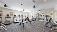 Located at 2880 Commonwealth Drive in Spring Hill, Tennessee, this fitness center offers a well-appointed exercise space designed to accommodate a comprehensive workout experience. The room features patterned, tile-cut carpet flooring throughout and is finished with clean white walls, crown molding, and multiple ceiling fans that ensure consistent airflow and comfort during workouts.

Natural light pours in through several large windows fitted with blinds, brightening the space and creating an open, inviting atmosphere. A full-length mirrored wall on one side visually expands the room while providing functional feedback during strength training.

The cardio zone is equipped with multiple treadmills and elliptical machines, each featuring individual display screens. A dedicated strength training area includes a multi-function cable machine, weight benches, and a well-stocked dumbbell rack with a full range of free weights. Additional equipment includes a seated resistance machine, medicine balls in various sizes, stability balls, and a cable attachment station. Wall-mounted flat-screen televisions are positioned throughout the room for entertainment during workouts.

Recessed lighting complements the natural light, and posted fitness center guidelines are displayed near the entrance. The space is thoughtfully organized to allow clear circulation between equipment zones, making it a functional and comfortable facility for a full range of fitness activities.