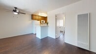 This single-floor unit offers a practical and well-organized layout designed for comfortable everyday living. The open living area is anchored by rich, dark hardwood-style flooring that runs throughout the space, paired with crisp white walls and a textured ceiling. A ceiling fan with a light fixture keeps the room comfortable, while a large window dressed with vertical blinds allows natural light to fill the room. A wall-mounted air conditioning unit provides additional climate control.

The kitchen is accessible via a peninsula-style breakfast bar that opens to the living area, creating a connected, social feel. Inside, warm wood cabinetry lines the walls from floor to ceiling, complemented by white countertops, a double stainless steel sink, a dishwasher, a gas range, and a microwave. The kitchen's galley configuration maximizes storage and functionality.

The bedroom is a quiet, well-proportioned retreat featuring the same dark hardwood-style flooring and a window that brings in ample natural light and outdoor views through vertical blinds.

The bathroom features a long vanity with white cabinetry and a wide mirror, offering generous counter and storage space. A separate water closet area includes a combination tub and shower with a sliding glass door, maintaining a clean and organized layout throughout.