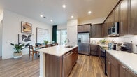 This single-story residence offers a thoughtfully designed open-concept layout with modern finishes and warm wood-look flooring throughout. The kitchen serves as the heart of the home, anchored by a central island with a built-in sink, stainless steel dishwasher, and crisp white countertops. Rich dark-stained cabinetry extends floor-to-ceiling, complemented by stainless steel appliances including a French door refrigerator with ice dispenser, a range, and an over-the-range microwave. Recessed lighting illuminates the space, while under-cabinet lighting adds a refined touch. The kitchen flows seamlessly into the dining area, where large sliding glass doors invite natural light and connect to outdoor views. A bright, welcoming hallway leads to the private quarters of the home. The primary bedroom features natural light from a large window, a sliding-door closet, and a spacious walk-in closet outfitted with multi-level shelving and hanging rods. The primary bathroom is equipped with a dual-sink vanity, dark wood cabinetry, and white countertops, brightened by a sizable window. Additional bedrooms are generously sized with ample natural light and closet storage. The cohesive design aesthetic, neutral palette, and consistent flooring create a harmonious and functional living environment throughout.