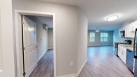 This single-floor, 3-bedroom, 1-bathroom residence offers a clean, modern aesthetic with consistent hardwood-style flooring and neutral gray-toned walls throughout. The open-concept kitchen and living area serves as the heart of the home, featuring a galley-style kitchen equipped with white shaker cabinets, light countertops, a full suite of black appliances including a range, microwave, dishwasher, and refrigerator, and a flush-mount ceiling light. The living area flows naturally from the kitchen and is brightened by multiple windows fitted with blinds and a ceiling fan overhead. Three bedrooms provide comfortable accommodations — the primary bedroom includes a wall-mounted mini-split HVAC unit and its own dedicated closet, while additional bedrooms feature natural light from windows and ceiling light fixtures. The full bathroom is finished with tile flooring, a white vanity with a quartz-style countertop, a mirrored medicine area, and a full tub-shower combination with chrome fixtures. Four closets, including wire-rack shelving systems, offer generous storage throughout. A dedicated laundry area includes washer and dryer hookups, rounding out this well-organized and move-in-ready home.
