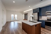 Located at 901 W 17th St in Kansas City, MO, this single-floor residence offers a thoughtfully designed open-concept layout filled with natural light. The contemporary kitchen is a standout feature, equipped with navy blue cabinetry, white quartz countertops, a stainless steel appliance suite including a refrigerator, range, and built-in microwave, and a subway tile backsplash. A central island with an integrated sink and pendant lighting anchors the space, flowing seamlessly into the expansive living area with rich hardwood flooring. A striking set of sliding barn doors adds an industrial-modern touch, separating the living space while allowing light to filter through the adjacent French doors. The bedrooms feature plush carpeting, ceiling fans, and generous natural light from large windows. The primary bathroom is appointed with a floating dual-sink vanity, wood-toned cabinetry, quartz countertops, large-format tile flooring, and a walk-in shower. A powder room with a wall-mounted sink provides added convenience. Additional highlights include an in-unit stacked washer and dryer with built-in shelving, recessed lighting throughout, and a clean, neutral color palette that complements the modern aesthetic of the home.