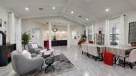 This single-floor community clubhouse offers a generously proportioned, well-appointed gathering space designed for both comfort and functionality. The interior is anchored by an open-concept layout that seamlessly connects several distinct zones, all unified by large-format polished tile flooring and a bright, white color palette accented with bold red décor throughout.

The main lounge area is defined by soaring vaulted ceilings with exposed beam detailing and recessed lighting, creating an airy, welcoming atmosphere. Comfortable gray upholstered seating arrangements, area rugs, and a wall-mounted television make this an ideal social hub. Natural light pours in through numerous windows dressed with white curtains, further enhancing the open feel. A secondary seating and conference area features a large central table with upholstered chairs, flanked by tall glass-paned doors that lead directly outdoors.

A dedicated reception and leasing counter is tucked toward the rear, featuring dark navy cabinetry, pendant lighting, and decorative map-print wall art — offering a professional yet inviting point of contact.

Adjacent to the main gathering area, the fitness center is well-equipped with treadmills, an elliptical, a rowing machine, a multi-function cable machine, free weights, and a weight bench. A wall-mounted television, ceiling fan, and rubber flooring complete this practical workout space.