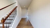 This two-story home offers a thoughtfully organized layout across two generously sized floors. The main level features an open-concept kitchen and living area anchored by a central island with granite countertops, cream cabinetry, stainless steel appliances, a subway tile backsplash, and recessed lighting. Rich hardwood flooring flows throughout the main level, complemented by abundant natural light from multiple windows. A compact bathroom on the main floor features a pedestal sink and oval mirror with chrome fixtures. A striking staircase with a warm wood handrail and decorative iron balusters connects the two levels, leading to a wide, clean hallway upstairs. The generously proportioned primary bedroom impresses with vaulted ceilings, plush carpeting, and direct access to an en-suite bathroom and a walk-in closet outfitted with wire shelving. Two additional bedrooms are carpeted and well-lit with large windows offering pleasant exterior views. An attached two-car garage with an automatic opener provides ample storage and parking. The home's neutral palette, quality finishes, and practical floor plan make it a functional and inviting residence suitable for a variety of lifestyles.