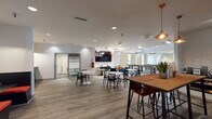 Located at 200 NC-54 E in Carrboro, North Carolina, this single-floor community clubhouse is designed to serve as a vibrant social hub. The space features an open, flowing layout with distinct zones that cater to a variety of activities and gatherings.

The main lounge area is anchored by a large wall-mounted flat-screen TV and furnished with plush cream and burnt-orange accent chairs arranged around a geometric-patterned area rug, creating a comfortable and stylish setting. A bold terracotta accent wall adorned with curated abstract artwork adds a warm, energetic focal point to the space, complemented by a cozy seating nook with blue upholstered chairs.

The game room boasts soaring vaulted ceilings and features both a full-size pool table and a shuffleboard table, illuminated by pendant track lighting. Large windows dressed with cream drapes allow ample natural light and offer views of the surrounding wooded landscape.

A dedicated dining and collaboration zone includes high-top bar tables and standard round tables with colorful seating, ideal for casual gatherings. The fully equipped kitchen presents white cabinetry with dark countertops, a hexagonal tile backsplash, stainless steel appliances, and a wood-top island table. Throughout the space, light wood-look flooring and bold patterned carpeting tie together a modern, eclectic aesthetic.