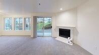 Located at 17525 NE 40th St in Redmond, WA, this single-floor, 2-bedroom, 1-bathroom residence offers a functional and well-organized layout. The combined living and dining area serves as the heart of the home, featuring plush carpeting, recessed lighting, and a classic white-mantled fireplace. A sliding glass door opens directly to a private patio, filling the space with natural light and providing views of the surrounding greenery. The kitchen is conveniently positioned adjacent to the living area, offering efficient use of space, and an in-unit laundry adds everyday convenience. Both bedrooms are carpeted and bright, each equipped with mirrored sliding closet doors that reflect natural light from the windows. The primary bedroom is generously sized, while the second bedroom also offers comfortable proportions and a window with outdoor views. Baseboard heating is present throughout the bedrooms. A central hallway connects all rooms, finished with neutral carpet and recessed lighting. The full bathroom features a clean, all-white tub and shower surround. Additional storage is provided by two dedicated closets. The overall aesthetic is neutral and move-in ready, with warm wood-toned door accents throughout.