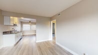 This single-floor residence offers a clean, contemporary aesthetic defined by light wood-tone flooring, neutral warm-beige walls, and crisp white trim found consistently throughout each room. The galley-style kitchen is a functional highlight, outfitted with white shaker cabinetry featuring gold-toned hardware, dark countertops, and a full suite of stainless steel appliances including a gas range, built-in microwave, refrigerator, and dishwasher. A ceiling fan and window at the end of the kitchen bring in natural light and airflow.

The open living and dining areas flow seamlessly together, providing a versatile and airy layout. Windows fitted with blinds allow natural light to filter in, while a wall-mounted AC unit ensures year-round comfort. The bedrooms are well-proportioned, each with light-filled windows and ceiling fans. One bedroom features built-in closet storage with shelving and a vanity mirror, adding practical utility.

The full bathroom is cleanly finished with white cabinetry, dark countertops with gold hardware, and a tub-shower combination enclosed by a sliding glass door with white tile surround. The floor plan, as seen in the dollhouse view, reveals a compact yet efficiently organized layout connecting all living spaces through a central corridor.