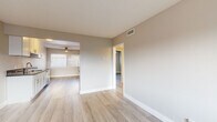This single-floor residence offers a clean, contemporary aesthetic defined by light wood-tone flooring, neutral warm-beige walls, and crisp white trim found consistently throughout each room. The galley-style kitchen is a functional highlight, outfitted with white shaker cabinetry featuring gold-toned hardware, dark countertops, and a full suite of stainless steel appliances including a gas range, built-in microwave, refrigerator, and dishwasher. A ceiling fan and window at the end of the kitchen bring in natural light and airflow.

The open living and dining areas flow seamlessly together, providing a versatile and airy layout. Windows fitted with blinds allow natural light to filter in, while a wall-mounted AC unit ensures year-round comfort. The bedrooms are well-proportioned, each with light-filled windows and ceiling fans. One bedroom features built-in closet storage with shelving and a vanity mirror, adding practical utility.

The full bathroom is cleanly finished with white cabinetry, dark countertops with gold hardware, and a tub-shower combination enclosed by a sliding glass door with white tile surround. The floor plan, as seen in the dollhouse view, reveals a compact yet efficiently organized layout connecting all living spaces through a central corridor.